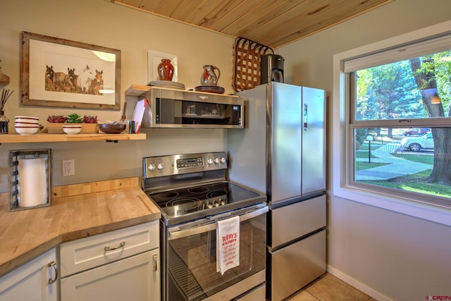 kitchen with butcher block counters, wood ceiling, stainless steel appliances, white cabinets, and light tile patterned floors