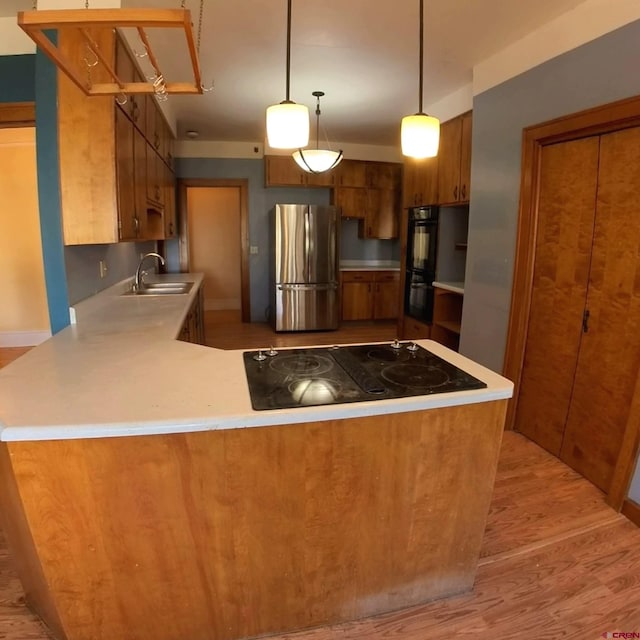 kitchen featuring black appliances, sink, kitchen peninsula, hanging light fixtures, and light hardwood / wood-style flooring