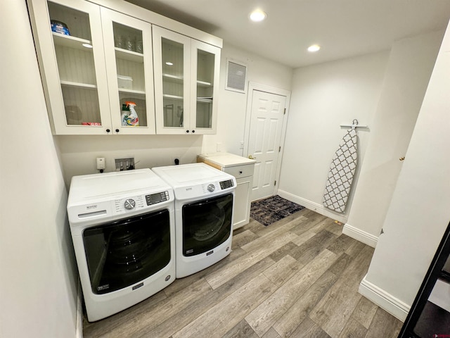 laundry area featuring light hardwood / wood-style floors, cabinets, and washing machine and clothes dryer