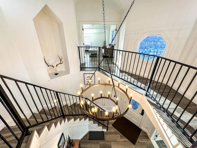 stairs with a towering ceiling, wood-type flooring, and an inviting chandelier