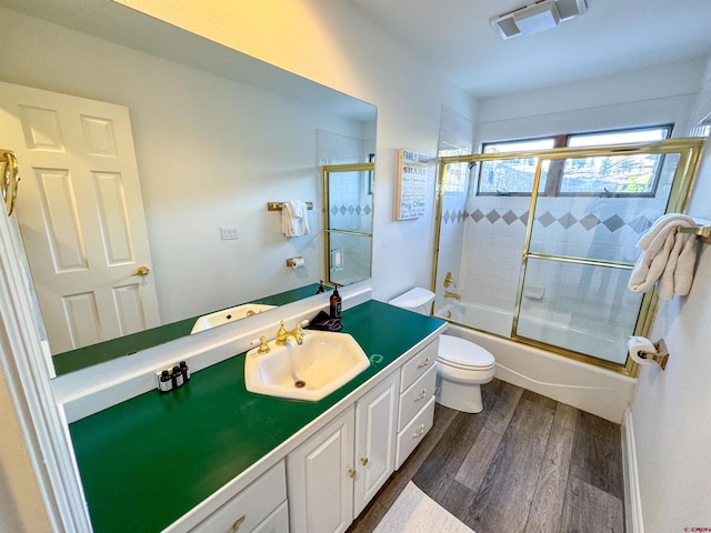 bathroom with vanity, enclosed tub / shower combo, toilet, visible vents, and wood finished floors
