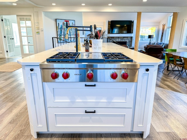 kitchen featuring white cabinets, a fireplace, light wood-type flooring, and an island with sink