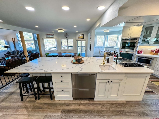 kitchen featuring a kitchen breakfast bar, white cabinetry, light stone counters, hardwood / wood-style flooring, and a kitchen island with sink