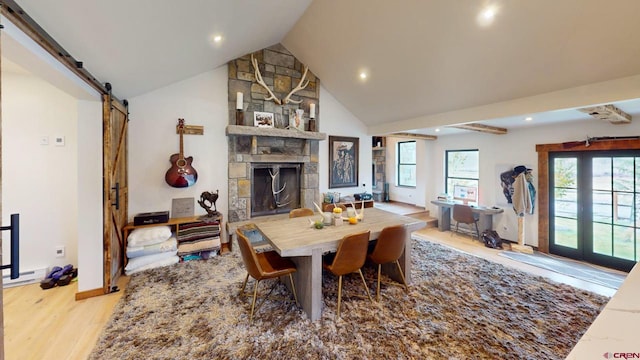 dining space with lofted ceiling, light hardwood / wood-style flooring, a stone fireplace, and a barn door