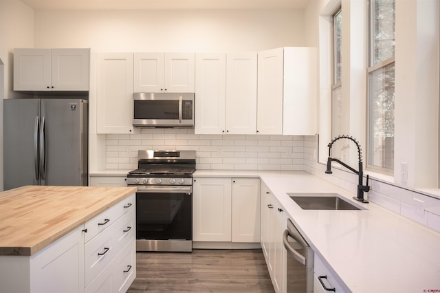 kitchen with white cabinetry, butcher block countertops, stainless steel appliances, and sink