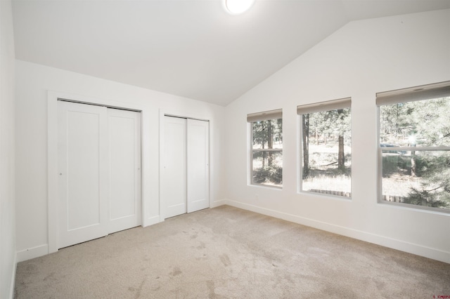 unfurnished bedroom featuring multiple closets, vaulted ceiling, and light colored carpet