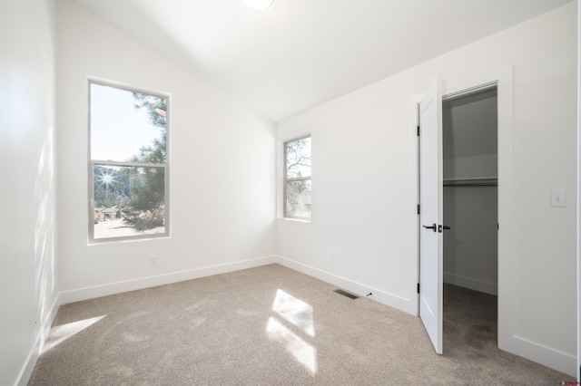 unfurnished bedroom with a spacious closet, lofted ceiling, multiple windows, and light colored carpet