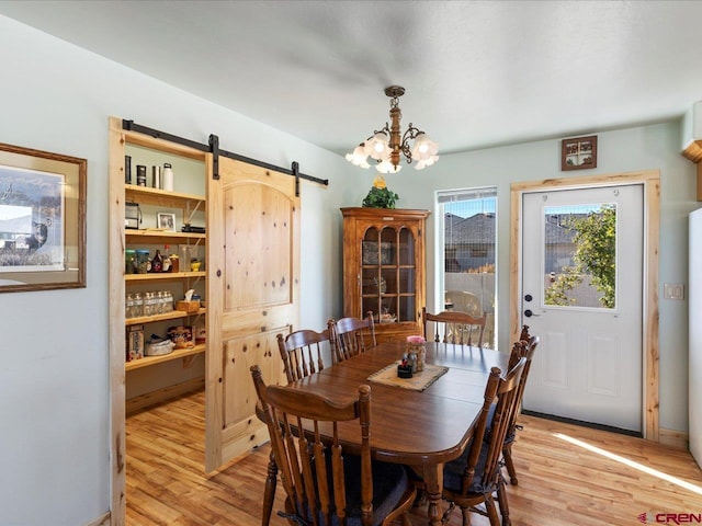 dining room with an inviting chandelier, a barn door, and light wood-type flooring