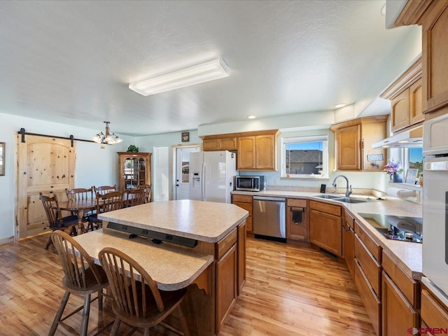 kitchen featuring appliances with stainless steel finishes, sink, a barn door, a center island, and light hardwood / wood-style flooring