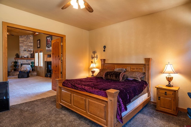 bedroom with dark carpet, a stone fireplace, and ceiling fan