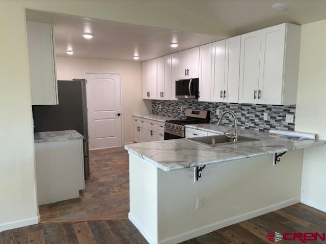 kitchen featuring a kitchen breakfast bar, white cabinetry, stainless steel range oven, and kitchen peninsula