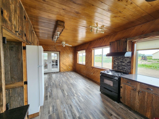 kitchen featuring black stove, white fridge, wooden walls, and dark wood-type flooring