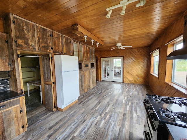 kitchen with white fridge, wood walls, stainless steel range with gas cooktop, and dark hardwood / wood-style flooring