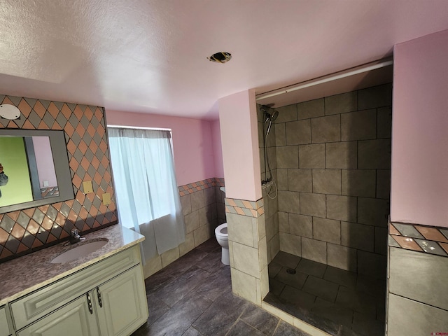 bathroom with a textured ceiling, toilet, tile walls, tiled shower, and vanity