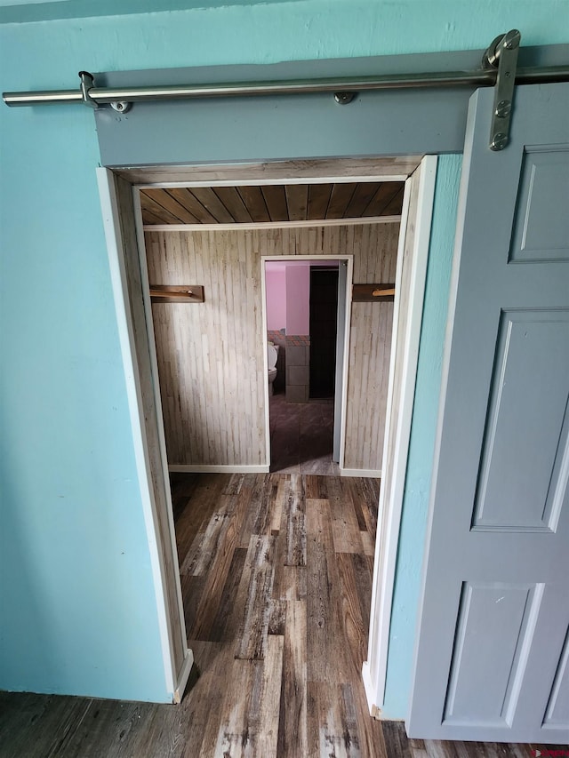 hall featuring dark wood-type flooring, a barn door, and wood walls