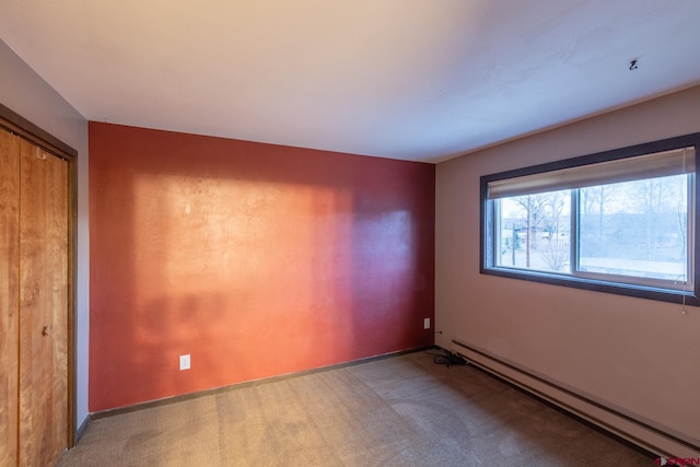 carpeted empty room featuring a baseboard heating unit