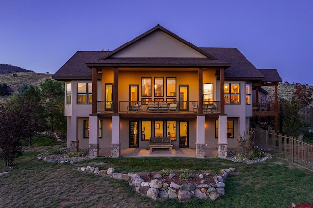 back house at dusk featuring a patio, an outdoor fire pit, a lawn, and a balcony