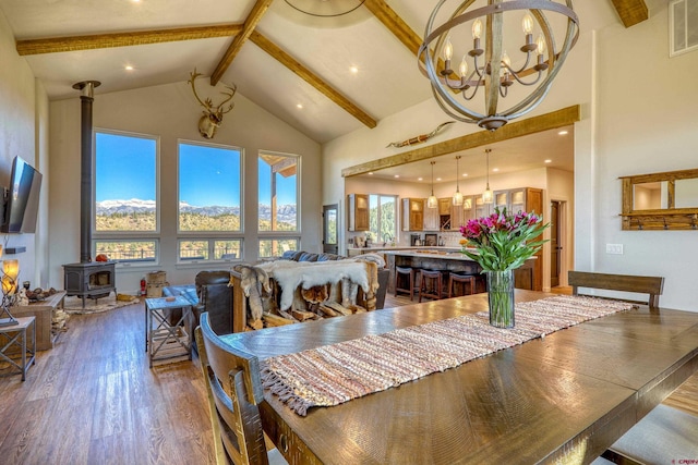 dining area with beamed ceiling, a mountain view, wood-type flooring, a wood stove, and high vaulted ceiling