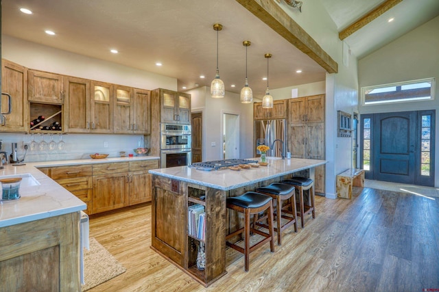 kitchen featuring appliances with stainless steel finishes, light wood-type flooring, hanging light fixtures, a breakfast bar area, and a kitchen island with sink