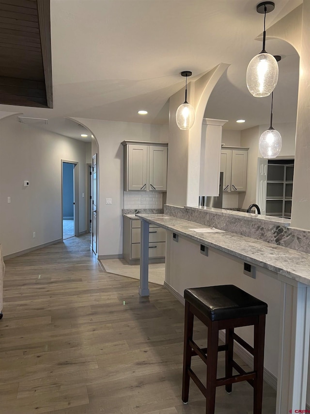 kitchen featuring light stone countertops, backsplash, a kitchen breakfast bar, decorative light fixtures, and dark hardwood / wood-style floors