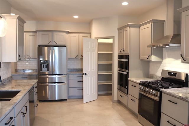 kitchen featuring appliances with stainless steel finishes, wall chimney exhaust hood, tasteful backsplash, and gray cabinets