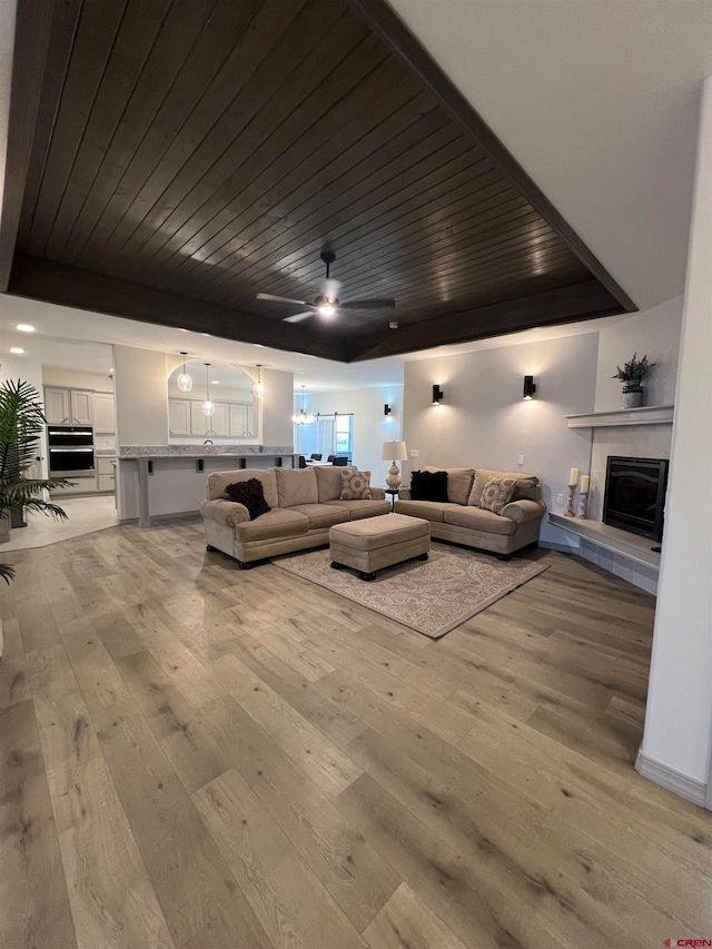 living room with a tile fireplace, wooden ceiling, light wood-type flooring, and ceiling fan