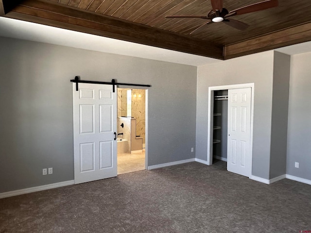 unfurnished bedroom with a closet, a barn door, wooden ceiling, and dark colored carpet