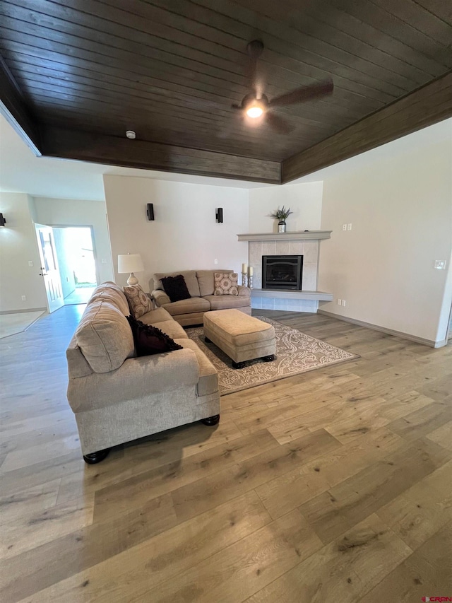 living room featuring light hardwood / wood-style flooring, wooden ceiling, and a tile fireplace