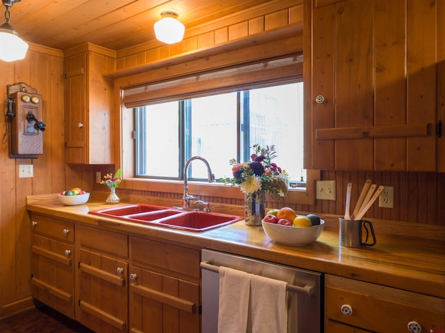 kitchen with stainless steel dishwasher, sink, pendant lighting, and wood walls