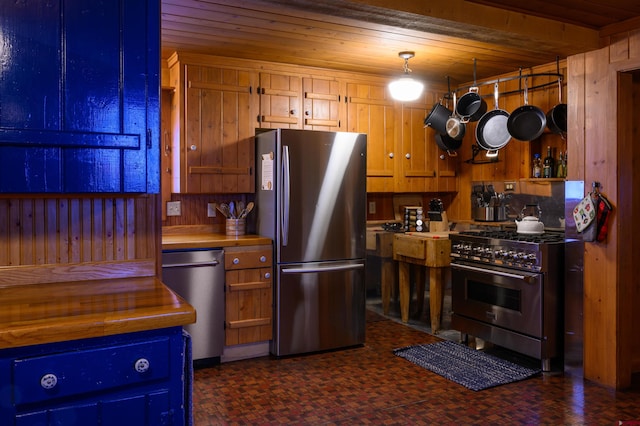 kitchen with wood ceiling, appliances with stainless steel finishes, hanging light fixtures, and wood walls