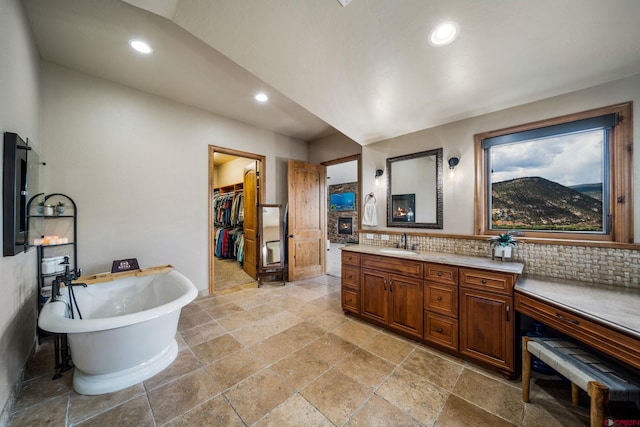 bathroom featuring stone tile flooring, recessed lighting, vanity, a freestanding bath, and a walk in closet