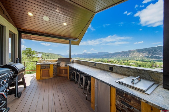 wooden terrace with an outdoor wet bar, a mountain view, a grill, and exterior kitchen