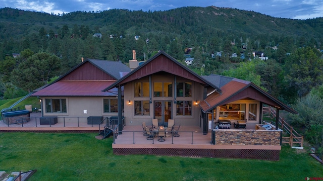 back of property featuring a view of trees, a deck with mountain view, a lawn, and stucco siding