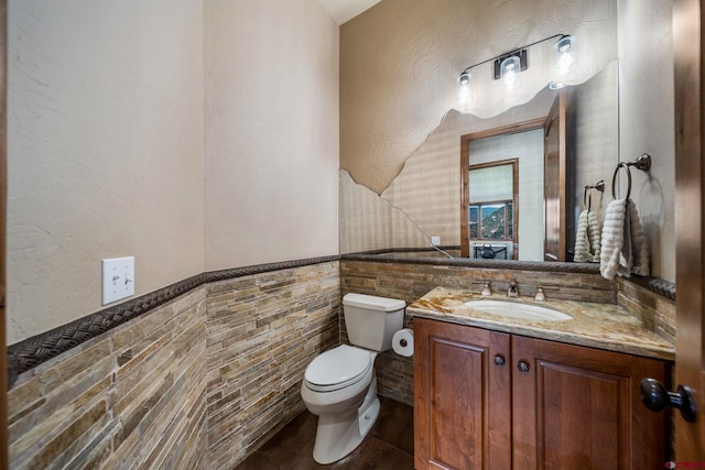 bathroom with toilet, tile walls, vanity, a wainscoted wall, and tile patterned floors