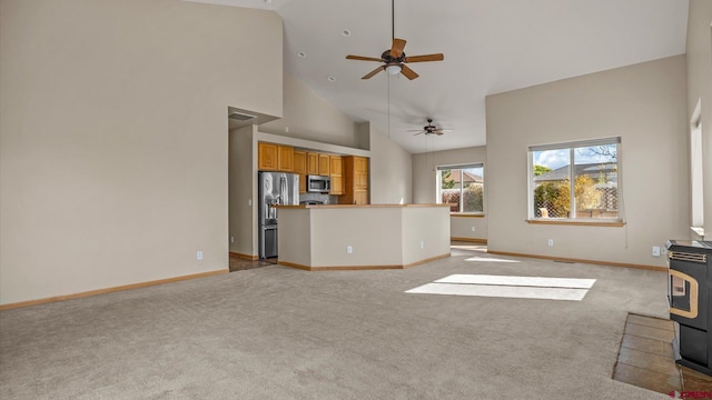 unfurnished living room with a wood stove, light carpet, high vaulted ceiling, and ceiling fan