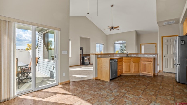 kitchen featuring a wood stove, sink, light brown cabinetry, appliances with stainless steel finishes, and high vaulted ceiling