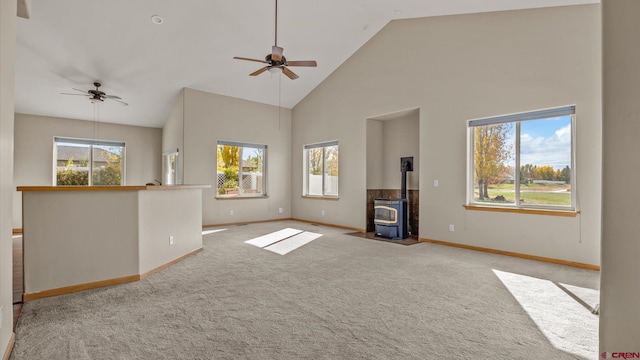 unfurnished living room with light carpet, a wood stove, high vaulted ceiling, and a wealth of natural light