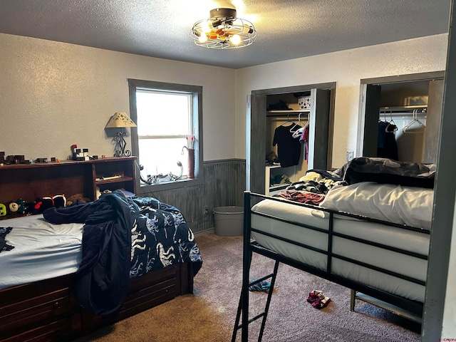 carpeted bedroom with wood walls, multiple closets, and a textured ceiling