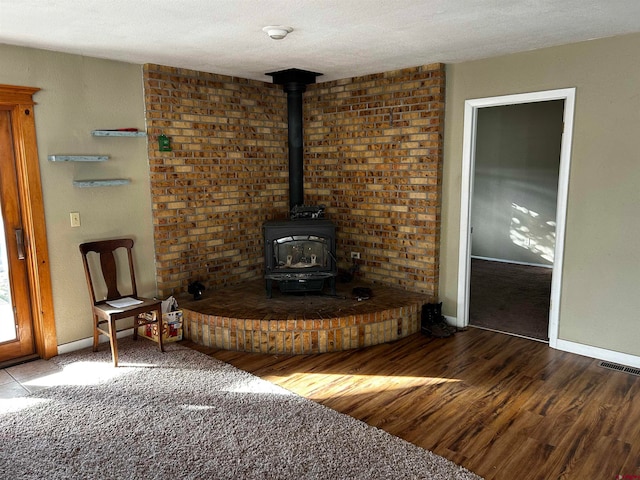 unfurnished living room featuring wood-type flooring, a textured ceiling, and a wood stove