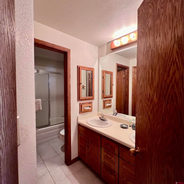 full bathroom with combined bath / shower with glass door, a textured ceiling, toilet, vanity, and tile patterned flooring