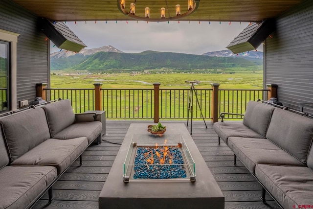 wooden terrace featuring a mountain view, an outdoor living space with a fire pit, and a rural view