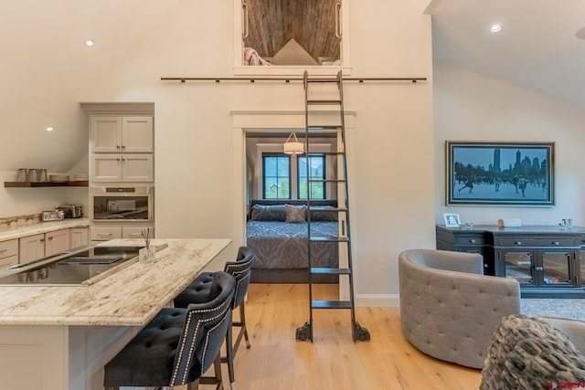 kitchen with hanging light fixtures, stainless steel oven, a kitchen breakfast bar, light wood-type flooring, and light stone counters