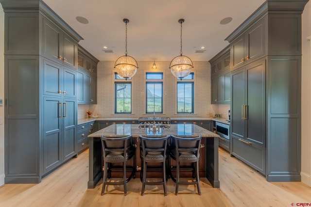 kitchen with a center island with sink, pendant lighting, and light wood-type flooring