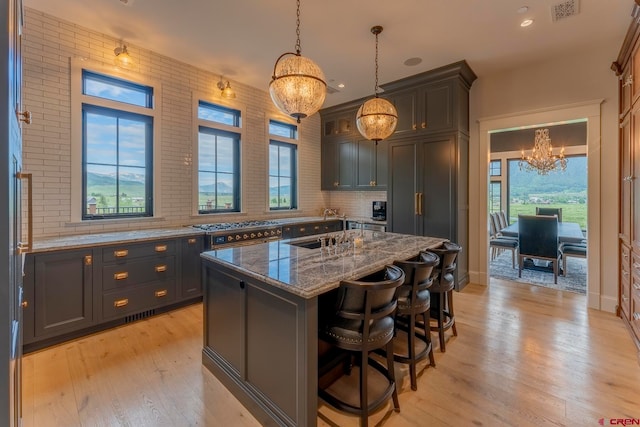 kitchen with hanging light fixtures, a breakfast bar area, a kitchen island, light wood-type flooring, and dark stone countertops