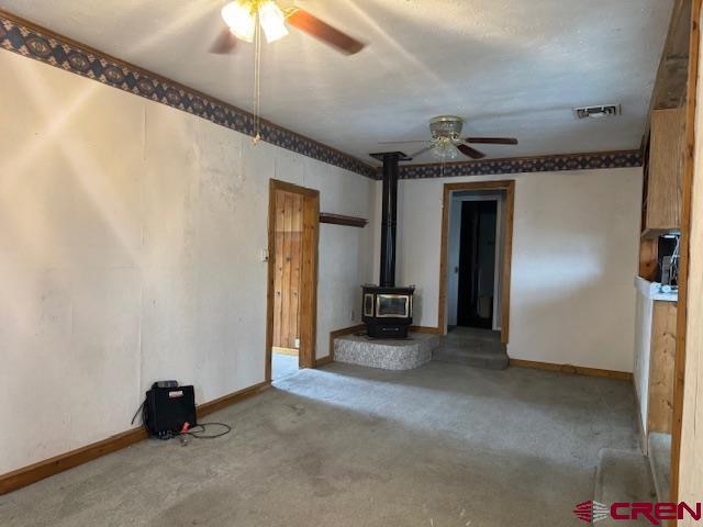 unfurnished living room featuring a wood stove, light carpet, and ceiling fan