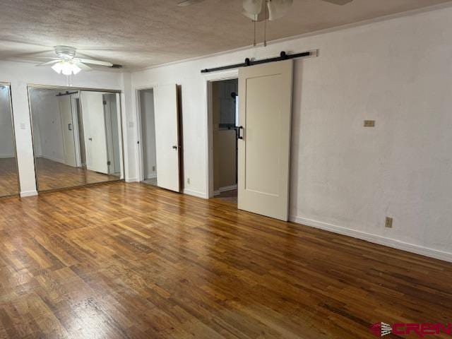 unfurnished room featuring hardwood / wood-style floors, ceiling fan, a barn door, and a textured ceiling