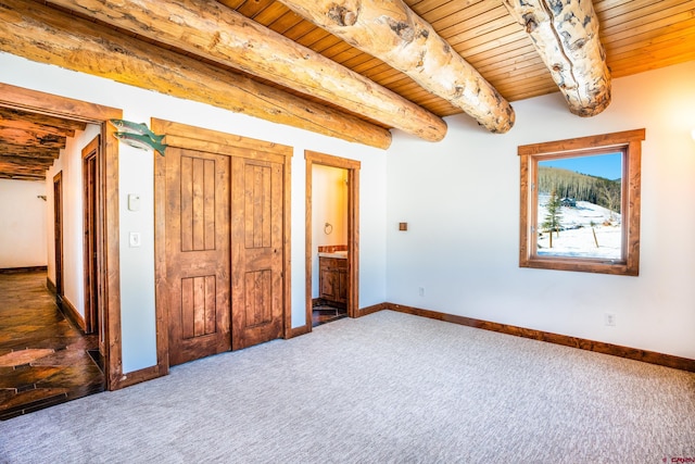 unfurnished bedroom with ensuite bath, beamed ceiling, dark carpet, and wooden ceiling