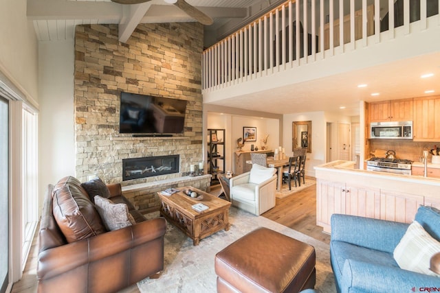 living room with a stone fireplace, high vaulted ceiling, beamed ceiling, ceiling fan, and light hardwood / wood-style flooring