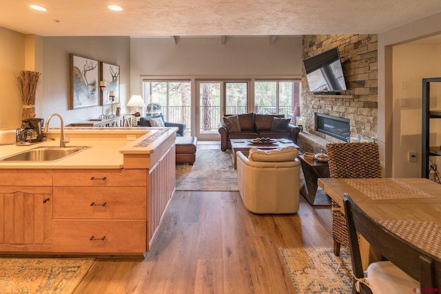 kitchen with a stone fireplace, light wood-type flooring, a textured ceiling, and sink