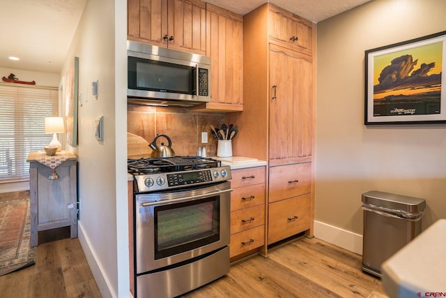 kitchen with stainless steel appliances, a textured ceiling, light wood-type flooring, and decorative backsplash